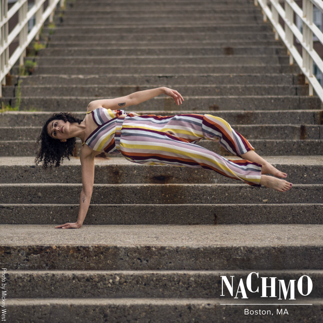 Woman in a striped jumpsuit with one hand on the landing to a cement staircase and the rest of her body parallel to the ground
